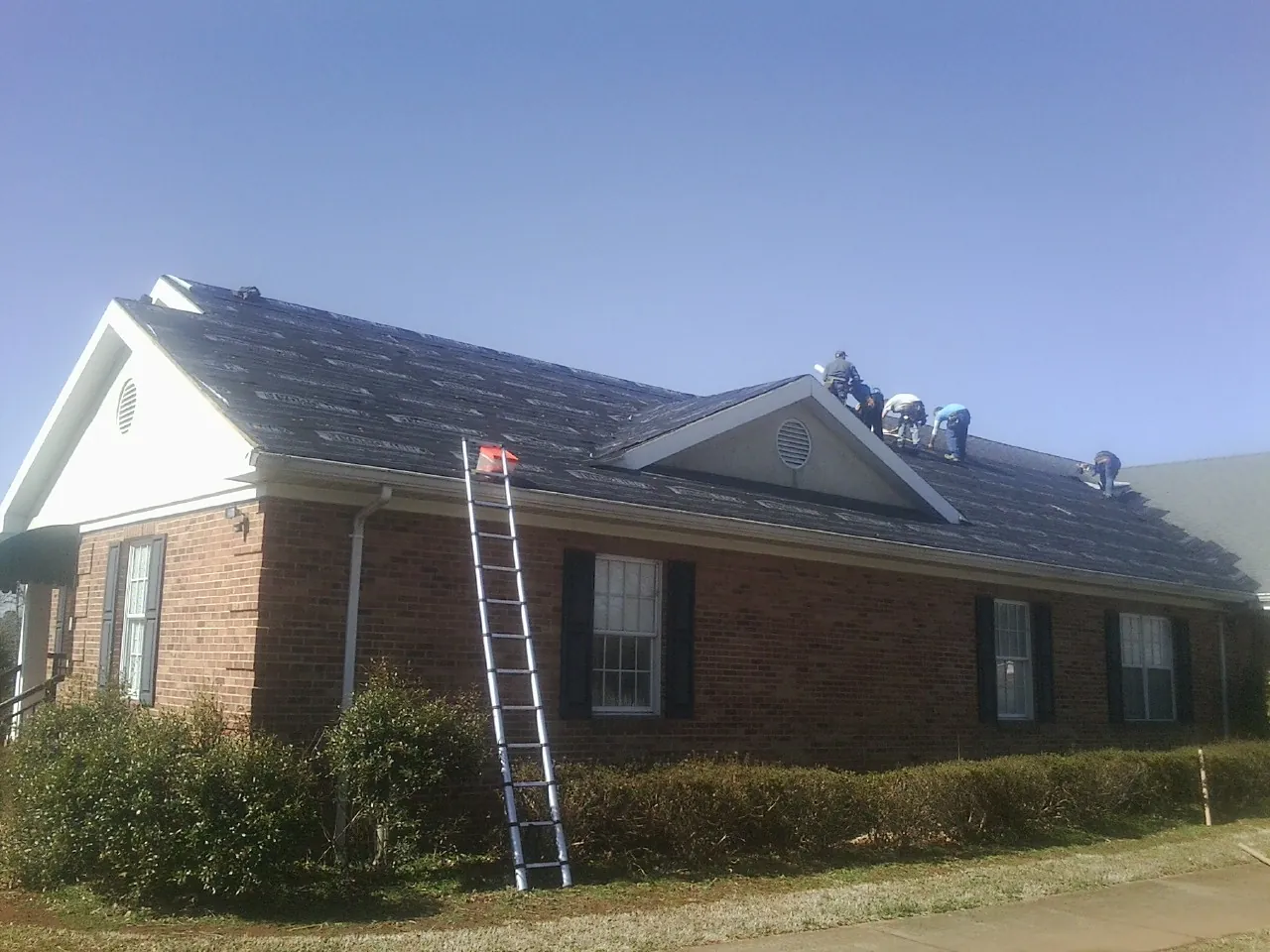 Crew tearing shingles off a brick ranch roof with a ladder set — Metal Roof Repair work by our crew in Oakesdale