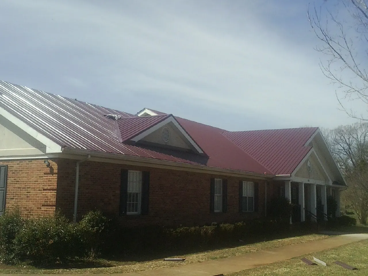 Red metal roof with gabled entries on a long brick building, from a Hail Damage Roof Repair job in Oakesdale