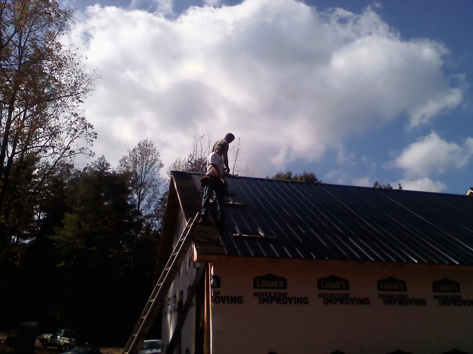 Roofer fastening dark metal panels high against a cloudy sky, from a Roof Inspection job in Oakesdale