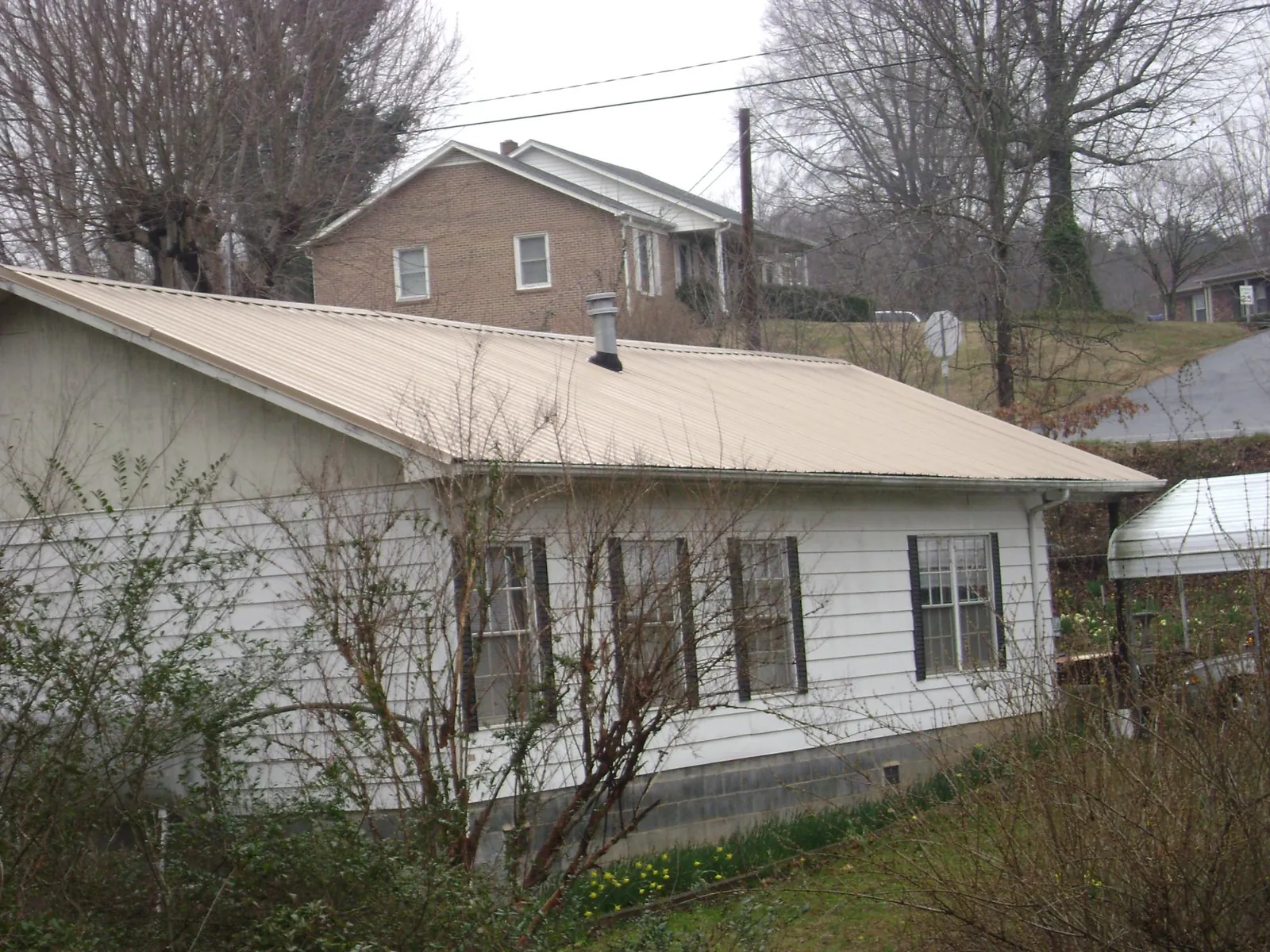 Tan metal roof on a white sided house set into a hillside — Commercial Roofing by Roofing Brothers in Oakesdale