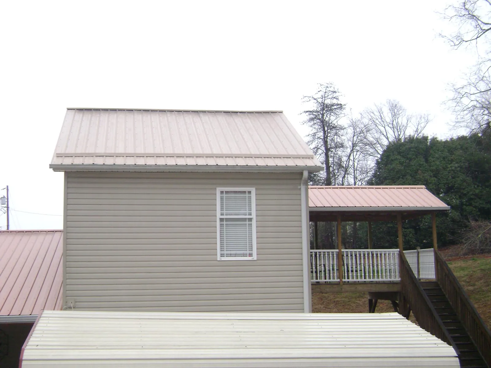 Tan metal roofs on a two story addition and attached porch, from a Roof Replacement job in Oakesdale